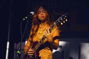 The Jesse Williams Band - a female guitarist dressed in yellow plays on stage at night.