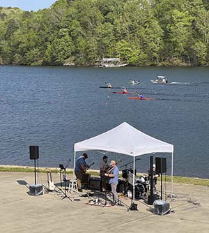 View of the band Six Foot Ramblers playing under a tent with Lake Lanier and LCKC paddlers in the background.