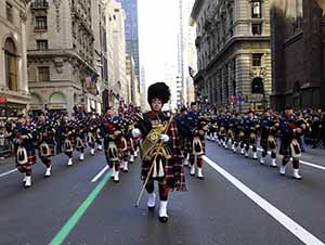 A wide view looking down the street at a nation-wide group of bagpipe players as they march and play bagpipes in New York's St. Patrick's Day Parade.