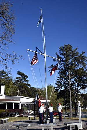 Three UYC members dressed in uniform standing around a flag pole raising flags.