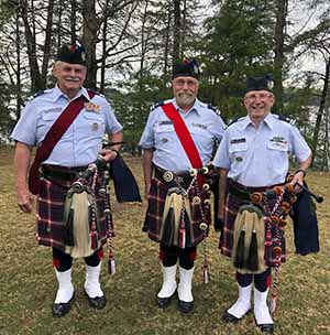 Three bagpipers standing outside dressed in traditional attire.