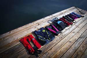 A row of different types and colors of life jackets laid out on a wooden dock.